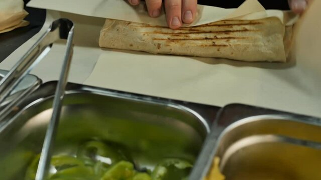 Close-up of the chef's hands put the cooked shawarma or doner kebab in pita bread in wrapping paper and professionally packaged for a fast food customer. Fast food restaurant