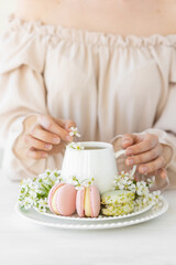 Traditional delicious French dessert - sweet homemade macarons on a vintage plate. Colourful tasty macaroons served on a white china with herbal tea. Decorated with fragile cherry tree flowers.