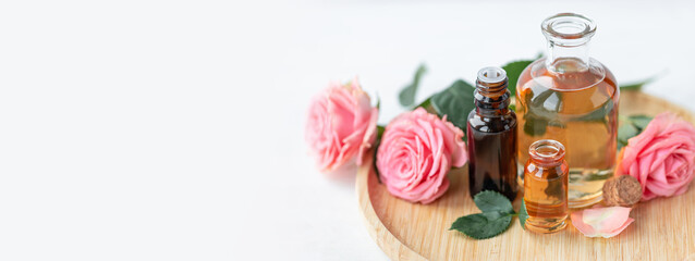 Aromatherapy. Pure organic essential rose oil concept. Elixir with plant based floral herbal ingredients. Pink flowers extract. Spa atmosphere with candle, towel. White background. Banner copy space