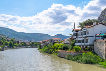 Fototapeta na wymiar View of old traditional Ottoman houses on the banks of Yesilirmak river in Amasya city. Amasya landscape beautiful river with clouds, sunny summer day. Popular tourist destination in Turkey