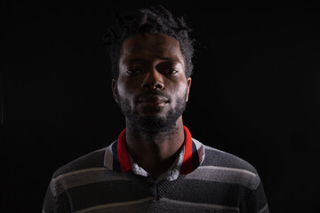 Serious young African man low key headshot on black background