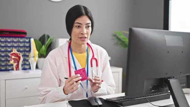 Young beautiful hispanic woman doctor writing medical report holding condom at clinic