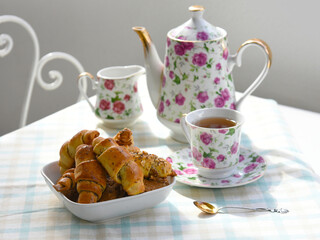 Pastry and cup of hot tea closeup. Tea party table setting, homemade nut rolls cookies, porcelain china set and antique tea spoon.Sunny day, fresh sweet baking goods, tasty tea break time concept. 