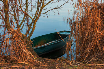Tin fishing boat anchored on the edge of a pond by the winter reeds.