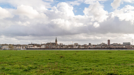 Fototapeta na wymiar Skyline of the city of Nijmegen, Netherlands with the river Waal in front and a field of grass on a cloudy day