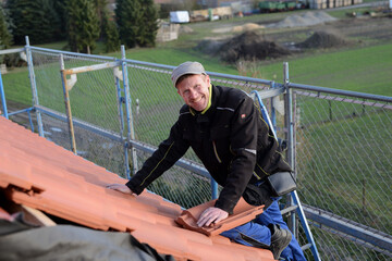 Freudiger Facharbeiter Dachdecker Geselle mit Spaß bei der Arbeit auf dem Ziegel Dach