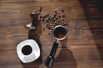 Naklejka premium a cup of coffee, coffee beans, a coffee horn and a tamper on a wooden background selective focus