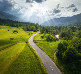 Aerial view of road in green meadows at sunset in summer. Top view from drone of rural road,...