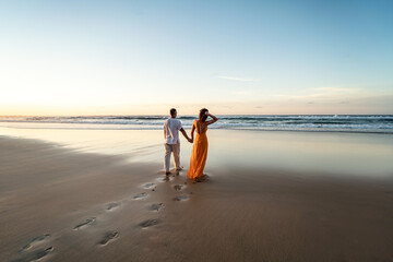 Romantic couple walking on sunset beach, enjoying evening light, relaxing on tropical summer vacation. Honeymoon. Love. Back view. - 585244299