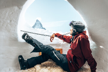 Portrait of smiling tourist snowboarder sitting inside an iglu dorf with a view on the famous...