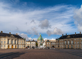 Fototapeta na wymiar Copenhagen, Denmark - September 13, 2010: wide view of Amalienborg circle with royal palaces and green dome of Frederiks church in back behind equestrian statue of king Frederik V. Blue cloudscape