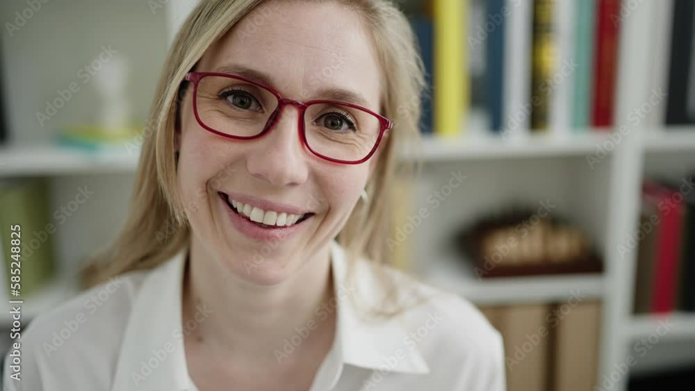 Poster Young blonde woman teacher smiling confident sitting on table at library university