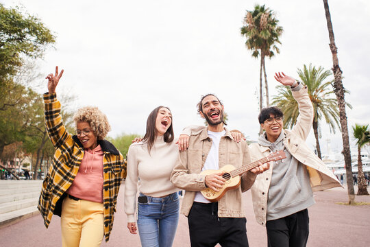 Happy people singing and dancing outdoors. Group of friends having fun in a day party playing the ukulele. High quality photo - Powered by Adobe