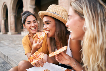 Three beautiful women sitting on the stairs of the city streets eating pizza from a street stall....
