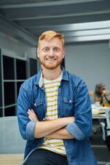 Vertical portrait of young red-haired programmer or businessman in a modern office looking camera...