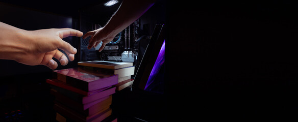 MANOS AGARRANDO LIBROS DENTRO DE UNA COMPUTADORA EN FONDO NEGRO, CONCEPTO DE TECNOLOGÍA Y...