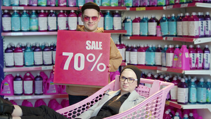 Fashionable modern man and woman looking at camera in fancy shop with 70 sale sign. rocker girl in...