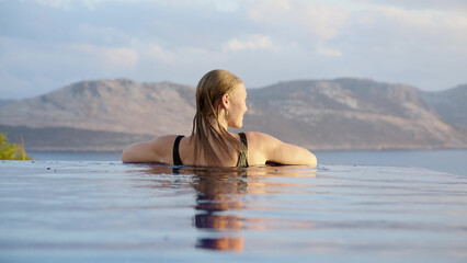 Silhouette of young unrecognizable woman at midday in infinity pool on edge of abyss. girl looks into distance, concept of loneliness and happiness to be alone for peace and tranquility.