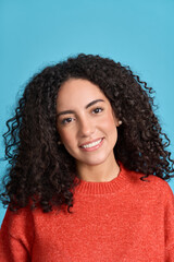 Young adult stylish pretty smiling latin woman, happy curly hispanic female model student wearing orange sweater standing looking at camera isolated on blue background, vertical headshot portrait.