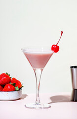 Bounty martini summer alcoholic cocktail drink with vodka, liqueur, cream, syrup, strawberries and ice in glass with cocktail cherry. Beige pink vanilla background