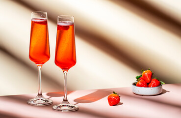 Rossini summer alcoholic cocktail drink with sparkling wine or prosecco, strawberry puree and ice in champagne glasses. Beige pink vanilla background, hard light, shadow pattern