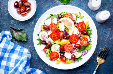 Greek salad with feta cheese, kalamata olives, red tomato, yellow paprika, cucumber and onion, healthy mediterranean diet food, low calories eating. Blue stone background, top view