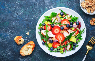 Strawberry, grilled chicken and herbs healthy salad with arugula, blueberries, avocado and walnuts, blue kitchen table. Fresh useful dish for healthy eating