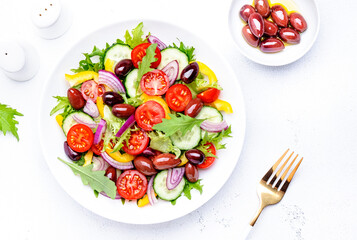 Vegan greek salad with kalamata olives, cherry tomato, yellow paprika, cucumber and red onion, healthy mediterranean diet food, low calories eating. White table background, top view