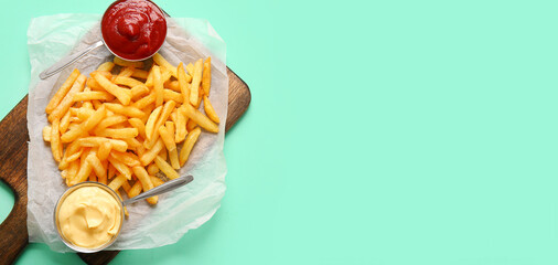 Tasty french fries and sauces on turquoise background with space for text