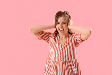 Angry young woman suffering from loud noise on pink background