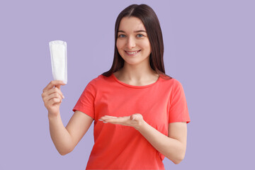 Young woman showing menstrual pad on lilac background