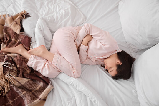 Young woman suffering from menstrual cramps in bedroom, top view