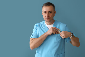 Mature doctor putting bribe in pocket on blue background