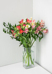 Glass vase with bouquet of beautiful alstroemeria flowers near light wall, closeup