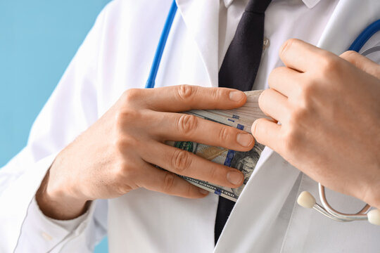 Male Doctor Hiding Bribe On Blue Background, Closeup