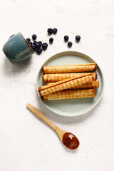 Plate of delicious wafer rolls with boiled condensed milk and blueberries on white grunge background