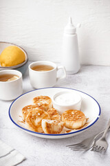 Plate with tasty cottage cheese pancakes, sour cream and cups of tea on light table