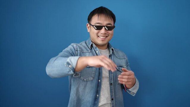 Young chinese man wearing thug life glasses throwing dollars over isolated blue background