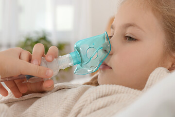 Little girl using nebulizer for inhalation in bedroom, closeup