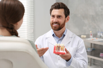 Doctor with educational model of dental implant consulting patient in clinic