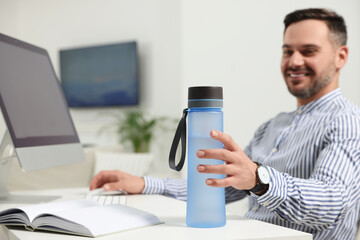 Man taking transparent plastic bottle of water while working in office, focus on hand