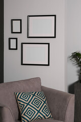 Empty frames hanging on white wall above armchair in room