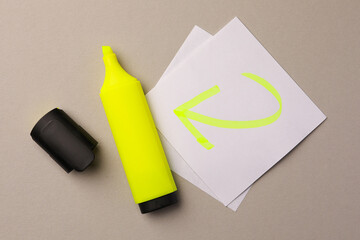 Bright yellow marker and sticky note with drawn arrow on light grey background, flat lay