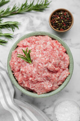 Bowl of raw fresh minced meat with rosemary and spices on white