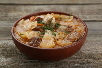 Tasty cabbage soup with meat, carrot and dill on wooden table, closeup