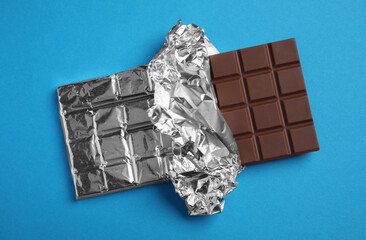 Delicious milk chocolate bar wrapped in foil on light blue background, top view