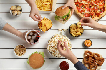 Friends eating burger, popcorn and other fast food at white wooden table, top view