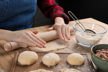 Woman rolling dough for chebureki at wooden table, closeup