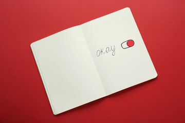 Notebook with word Okay and drawing of switch on button against red background, top view