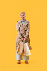 Fototapeta premium Beautiful mature woman with shopping bags on yellow background